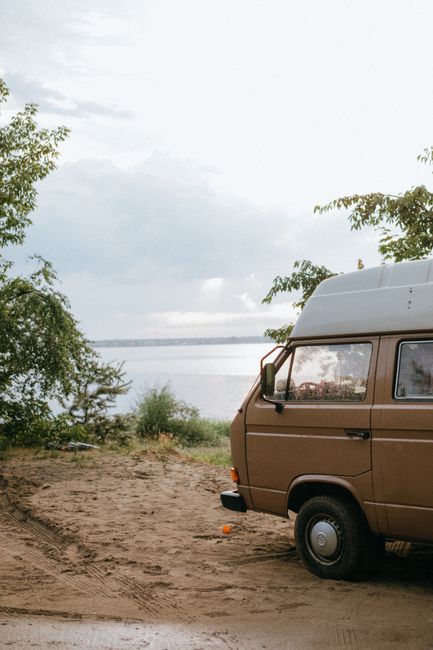 A black-and-white photograph showing a small white van parked on a flat, open area of sandy terrain, which is likely part of a natural landscape. The van is positioned near the centre of the image and