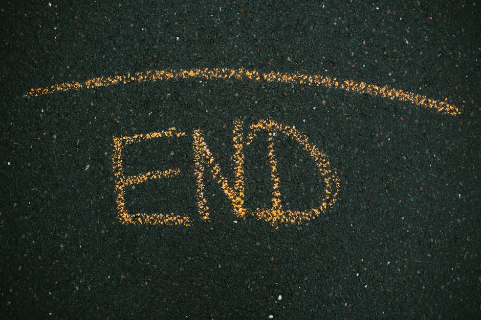 A close-up view of yellow chalk markings on a dark asphalt surface, with the letters and symbols 'EO' and an arrow drawn for parking or loading instructions. The surface appears to be part of a street or parking area, possibly in a residential or urban setting. The chalk markings are used to indicate specific areas for vehicle parking or loading zones, which may relate to house removals or relocation services provided by Man with Van Sands End. The background shows a textured, granular asphalt surface with small stones embedded within, illuminated by ambient lighting that highlights the contrast between the yellow chalk and the dark ground, suggesting an outdoor environment suitable for moving logistics and furniture transport preparations.